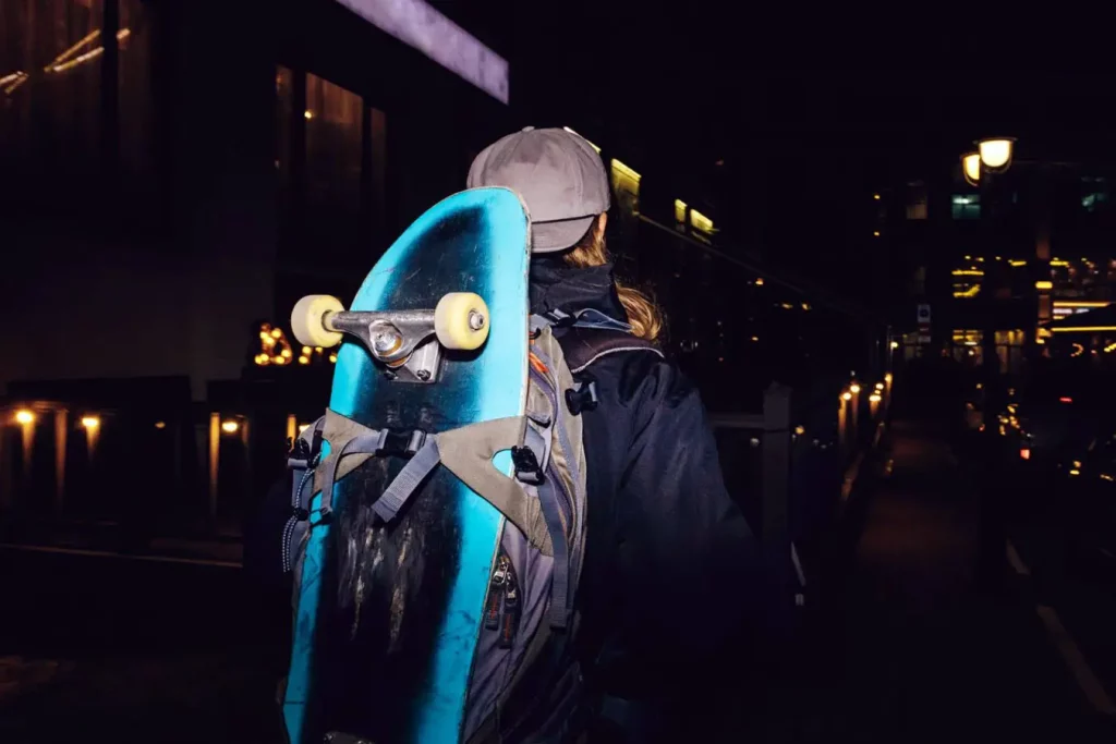Vertical method: Man with backpack carrying skateboard at night