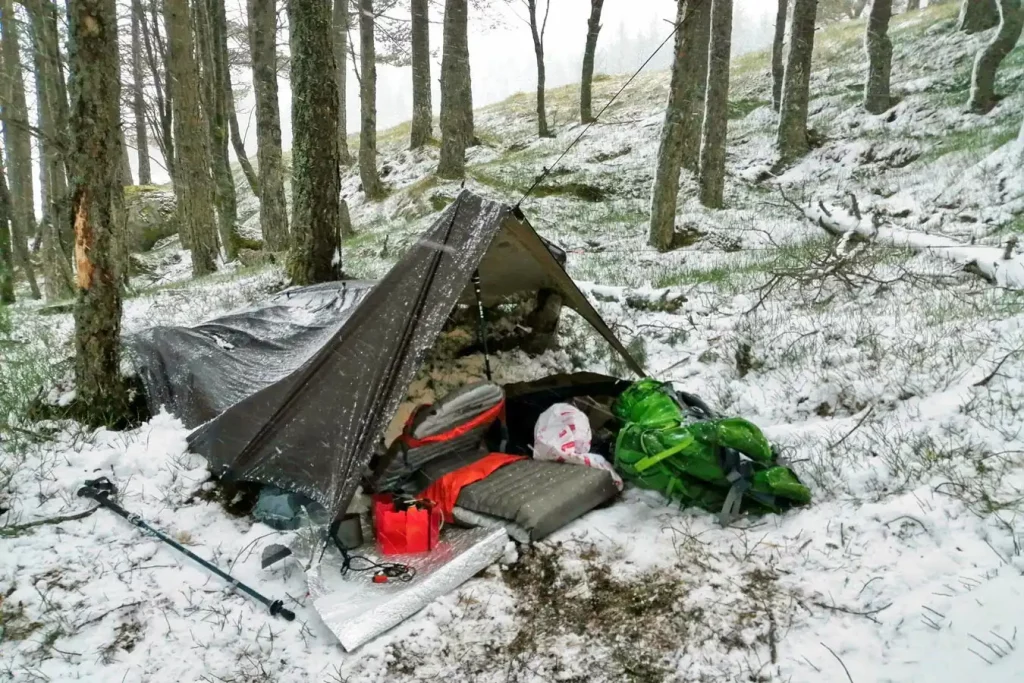 A tarpaulin and bivvy bag is pitched in the snow
