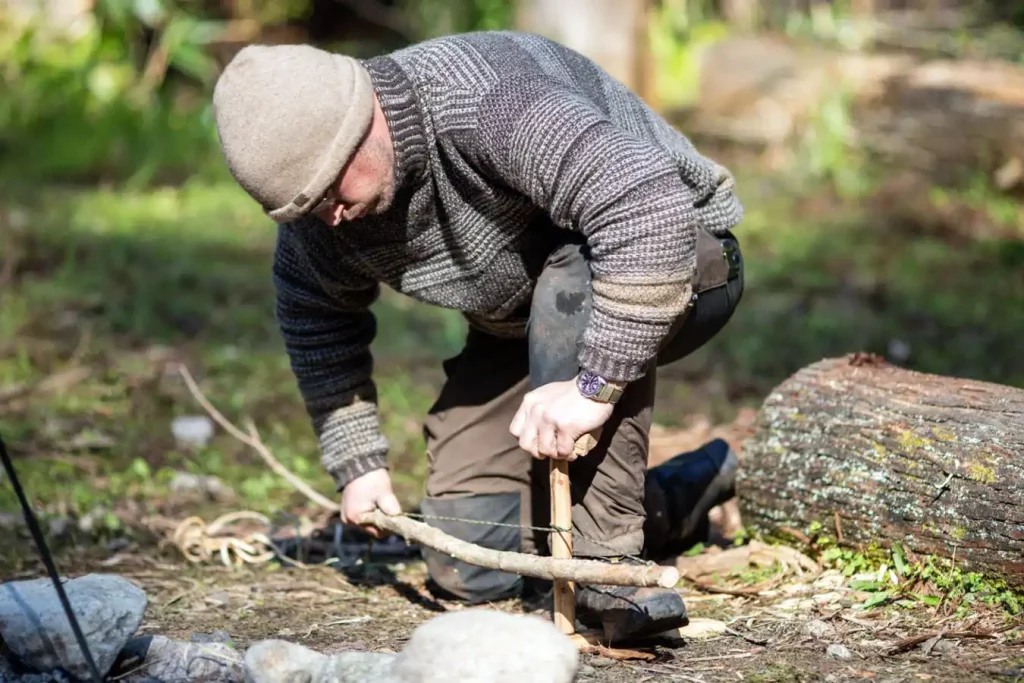 A skilled outdoorsman starting a fire with a bow drill made in the woods